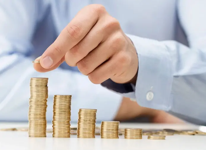 A person is putting money in stacks of coins.